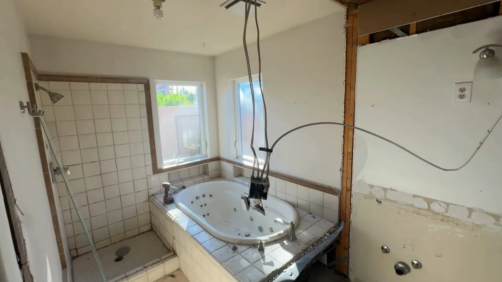 Bathroom stripped for a remodel with a jetted tub, tiled shower wall and an open wall