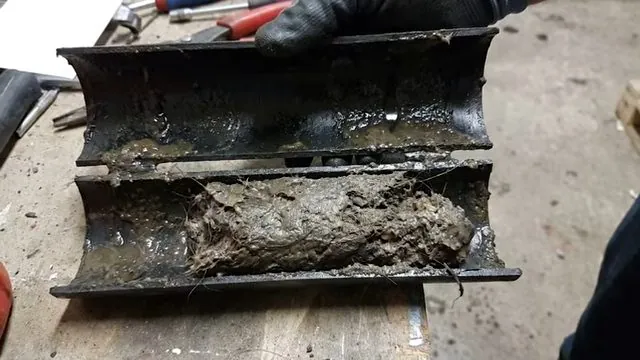 Cut open section of pipe lined with gray sludge on a workbench