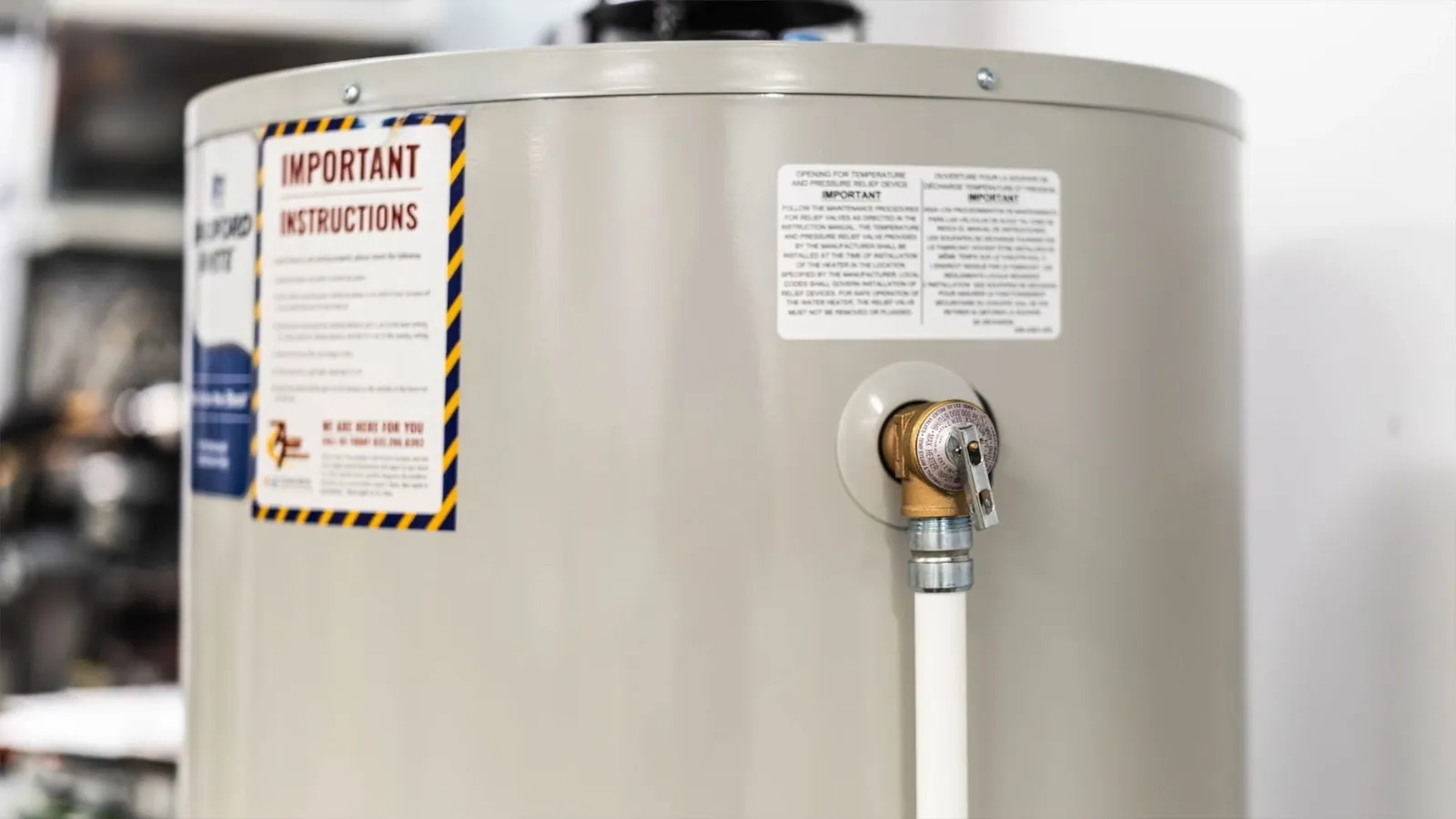 Beige water heater tank with an instruction label and a valve on a white pipe at its side