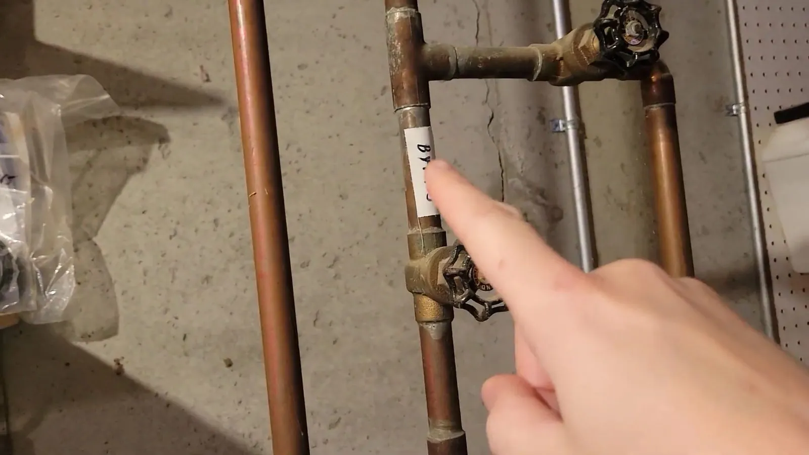 Finger pointing at copper pipes and a valve on a basement wall