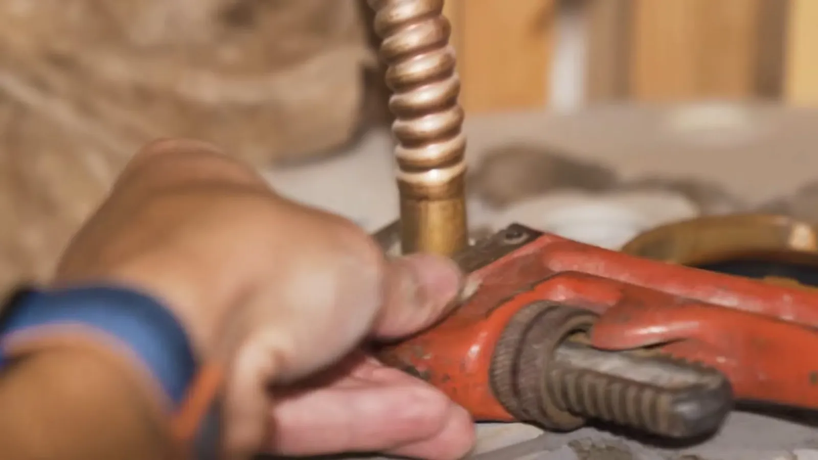 Hand gripping a red pipe wrench on a corrugated copper supply line