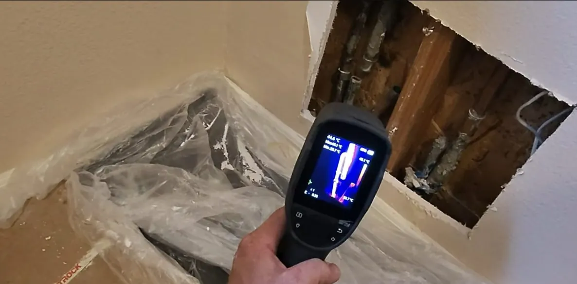 Hand holding a thermal imaging camera up to an opening cut in a wall