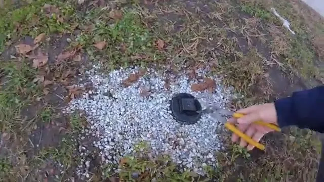 Hand with a pencil pointing at a cleanout cap set in a bed of gravel