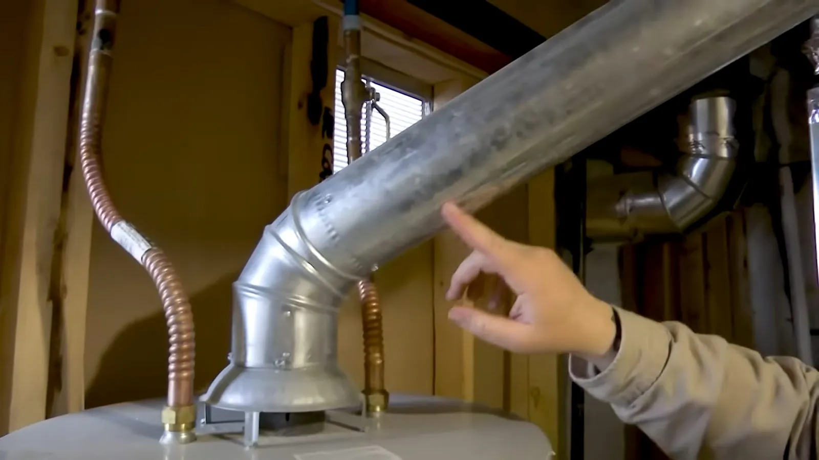 Hand pointing at a metal flue vent running above a water heater