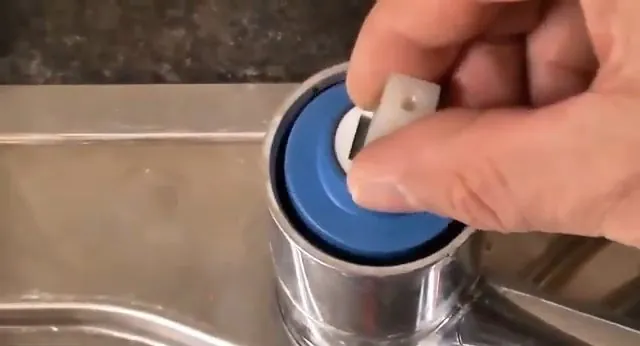 Hand lifting a faucet cartridge with a blue ring out of a chrome sink faucet