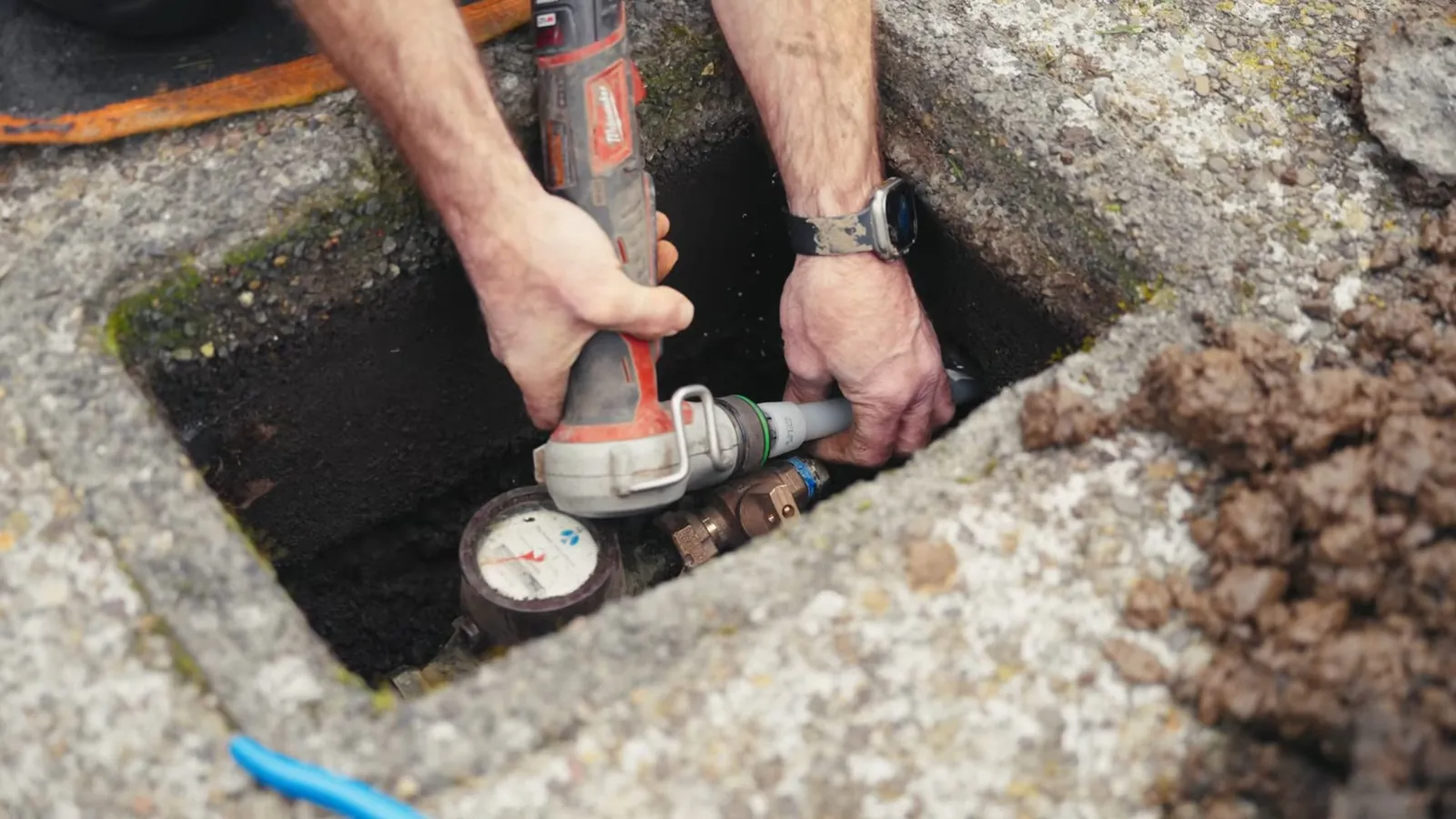 Hands working on a water meter and valve inside a concrete meter box