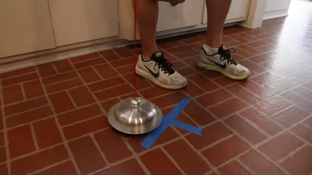 Legs in sneakers standing beside a silver dome sensor on a red tile floor marked with blue tape