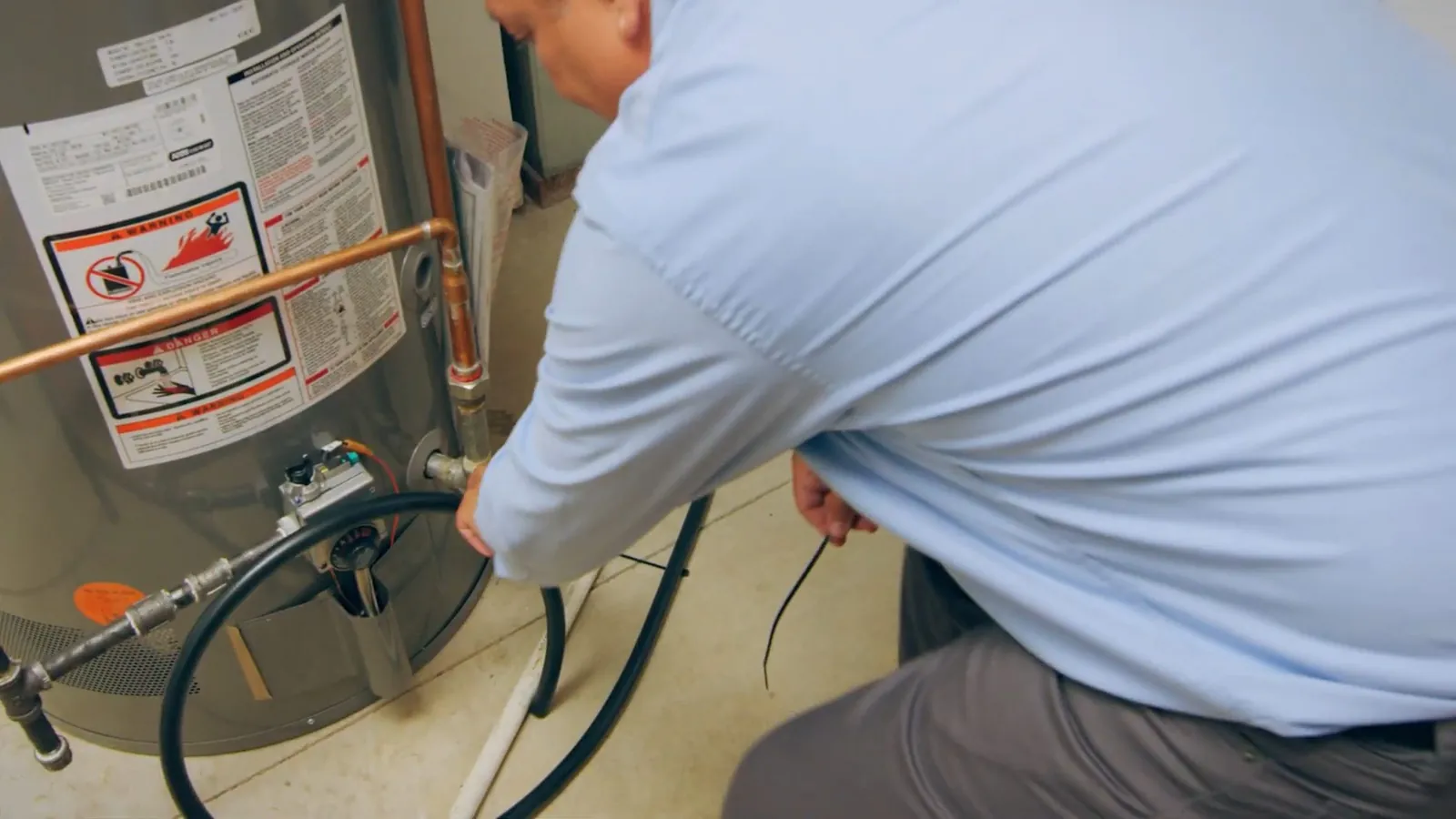 Plumber crouching beside a gas water heater and working at the pipe connections near its base