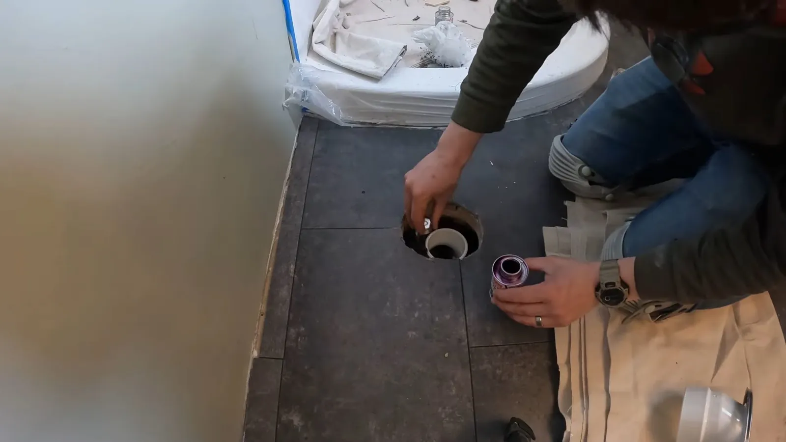 Man kneeling on a bathroom floor beside an open toilet flange and drain pipe