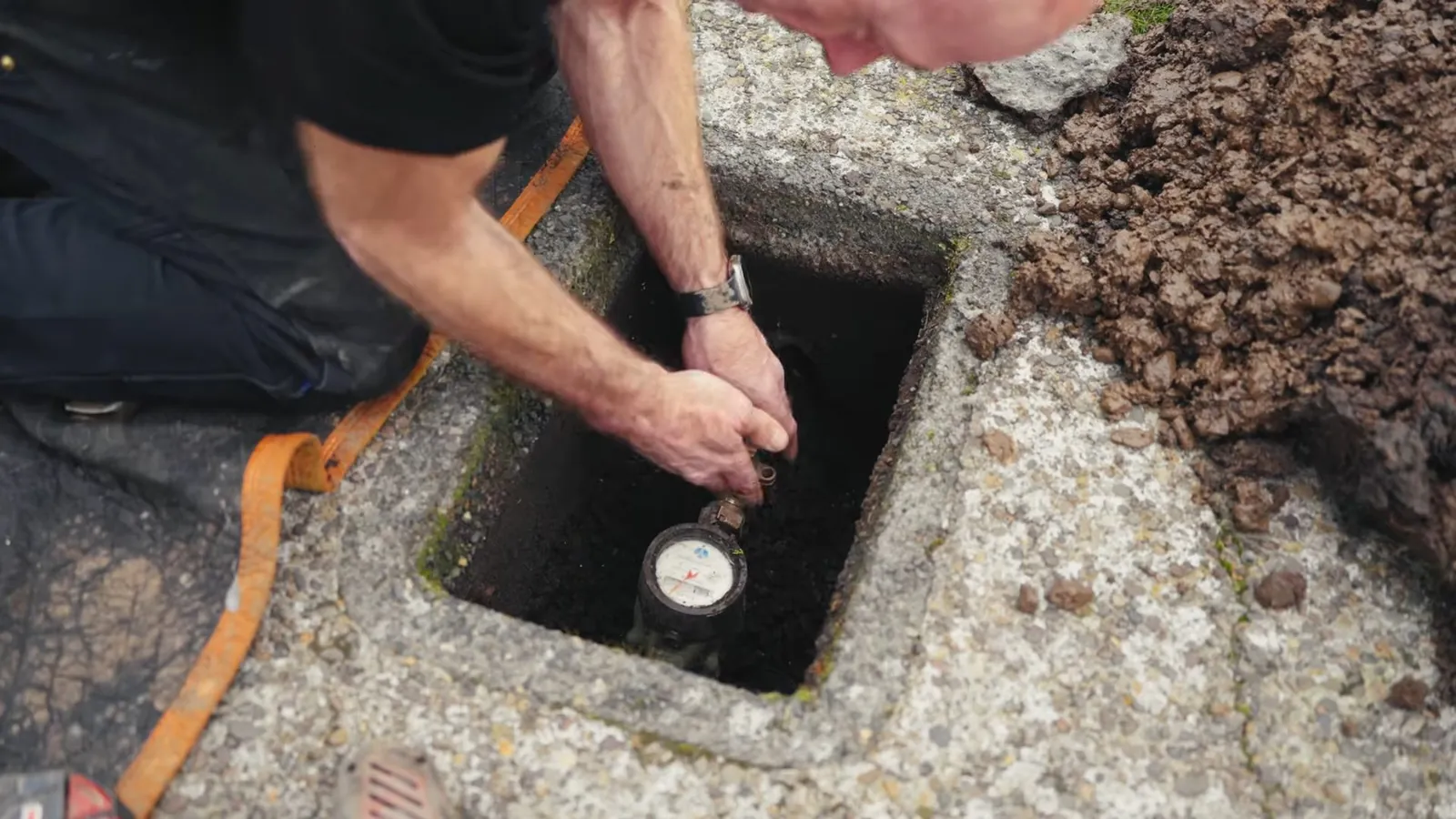 Man kneeling beside an open water meter box set in a concrete pad, reaching down to the meter