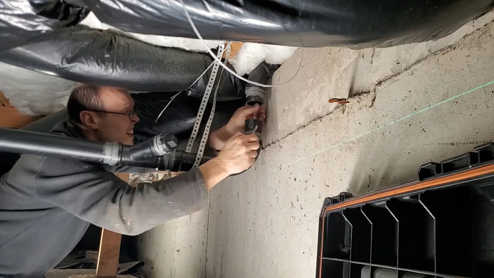 Man reaching up to work on pipes in a ceiling space beside a concrete wall and ductwork