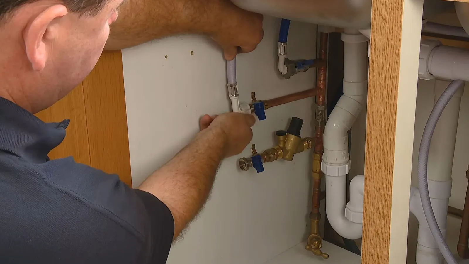 Man reaching under a sink to work on the shutoff valves and supply lines