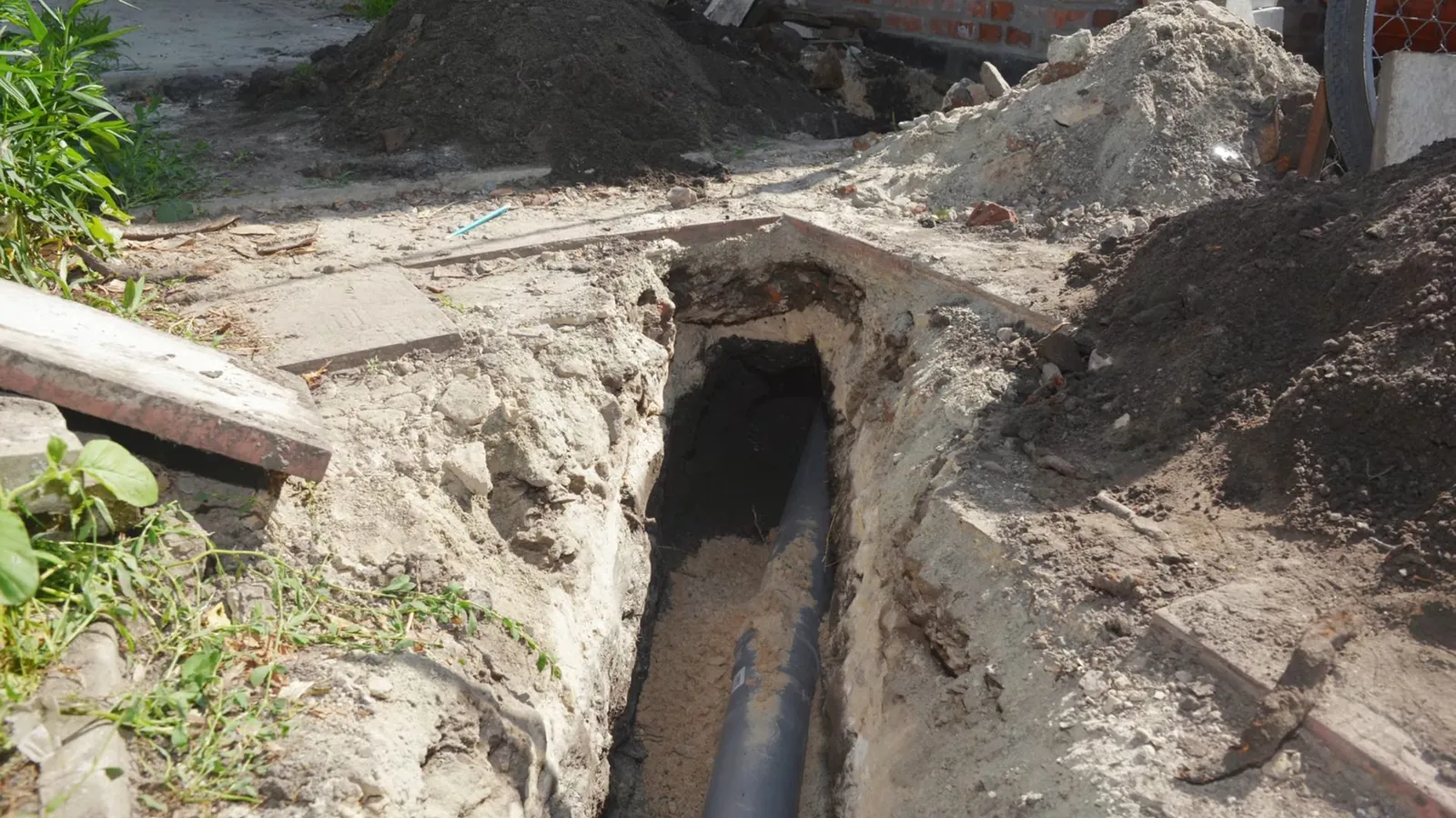 Narrow trench with a black pipe at the bottom and a pile of dirt beside it