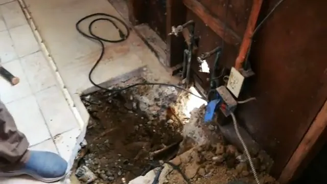 Opened floor and wall in an old bathroom with exposed pipes and a cord on the ground