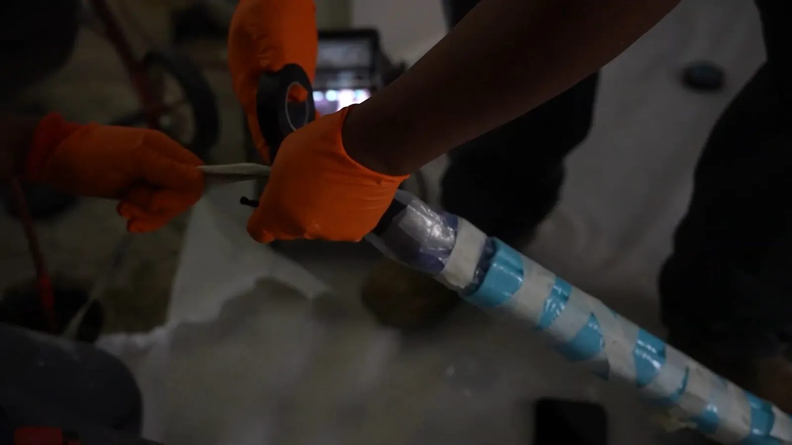 Orange gloved hands feeding a blue taped liner into a pipe