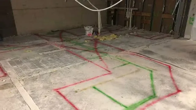 Paint markings in red and green showing utility lines on a bare concrete slab