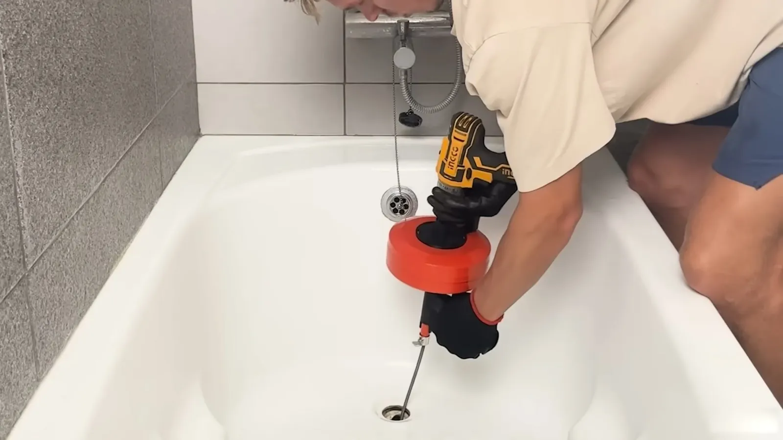 Person feeding a drain snake into a bathtub drain with a cordless drill