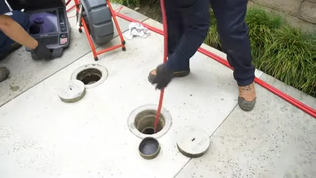 Plumber feeding a drain cable into a concrete cleanout with a camera reel beside it