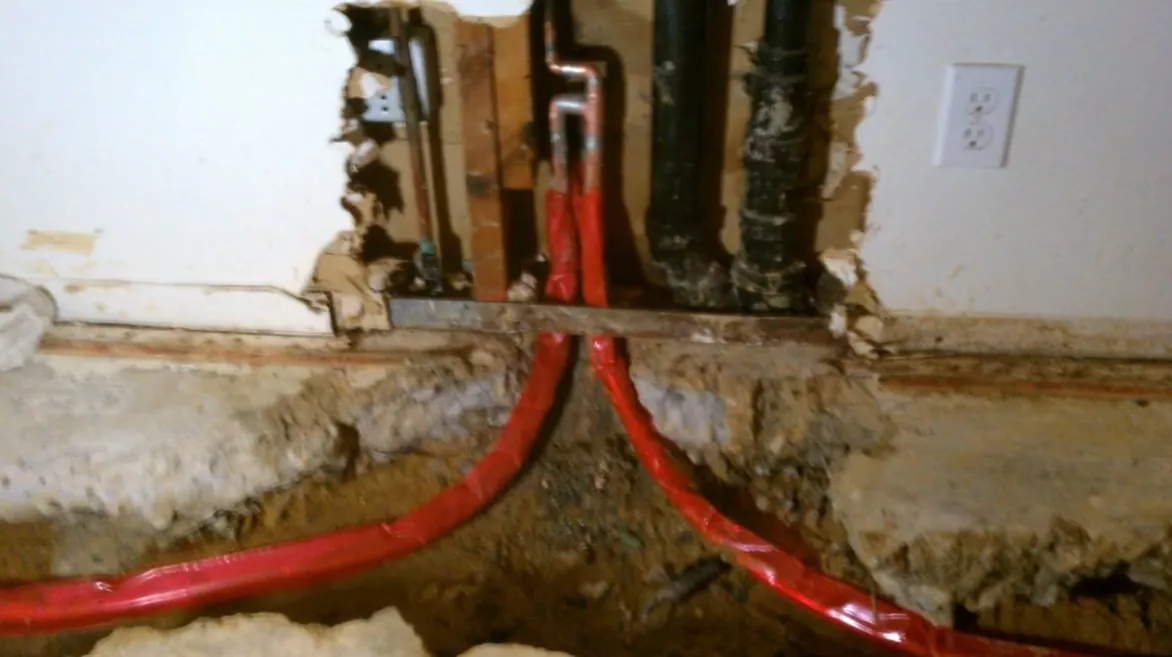 Red PEX lines running through an opened wall and into a trench in the slab