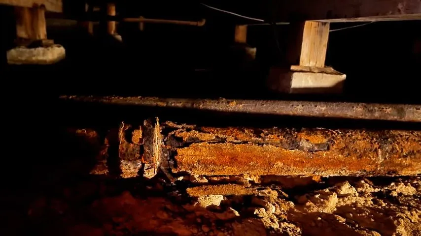 Rusted cast iron drain pipe running under floor joists in a crawlspace