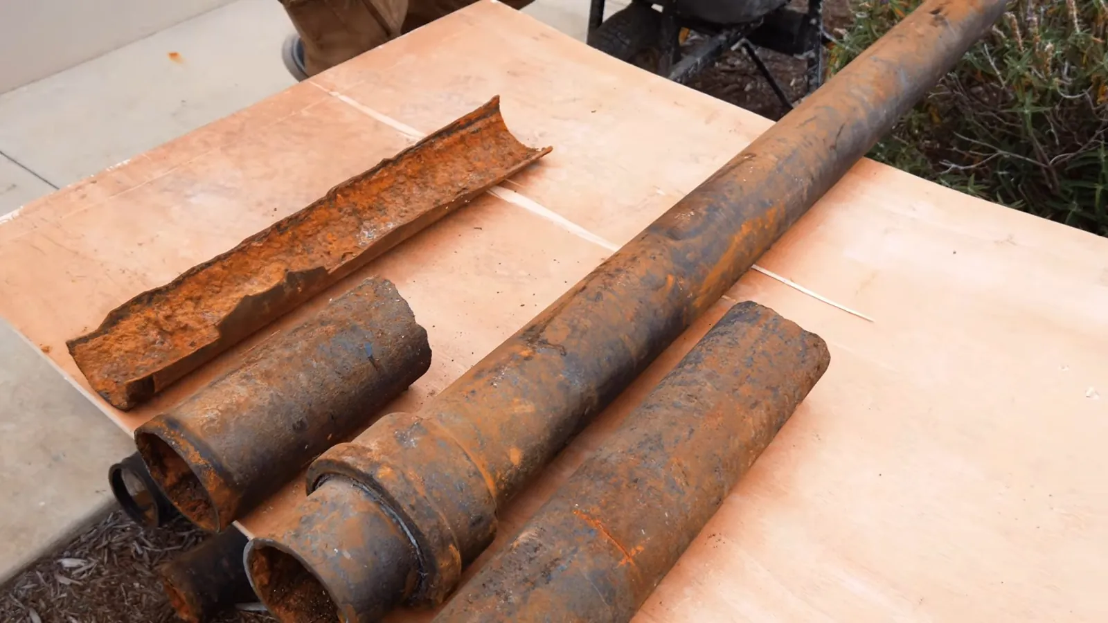 Rusty steel pipe sections, some cut open, laid on a wooden board