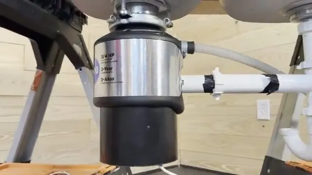 Stainless garbage disposal hanging under a double kitchen sink with white drain pipes
