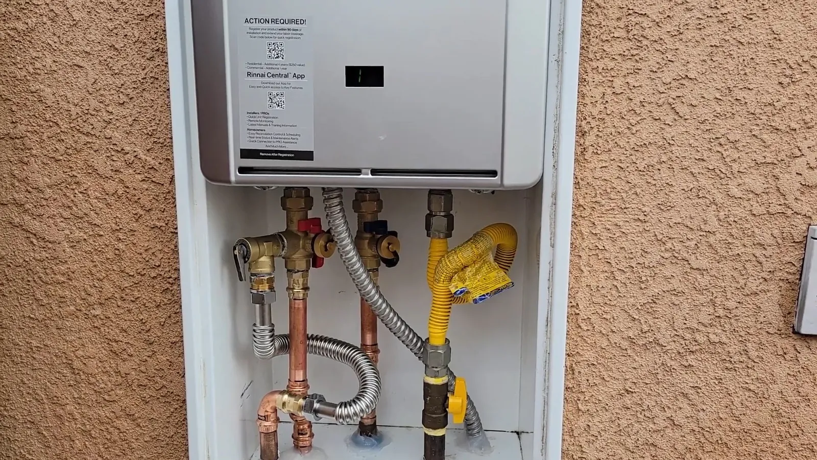Tankless water heater set in a recessed cabinet in a stucco wall with gas and water lines beneath it