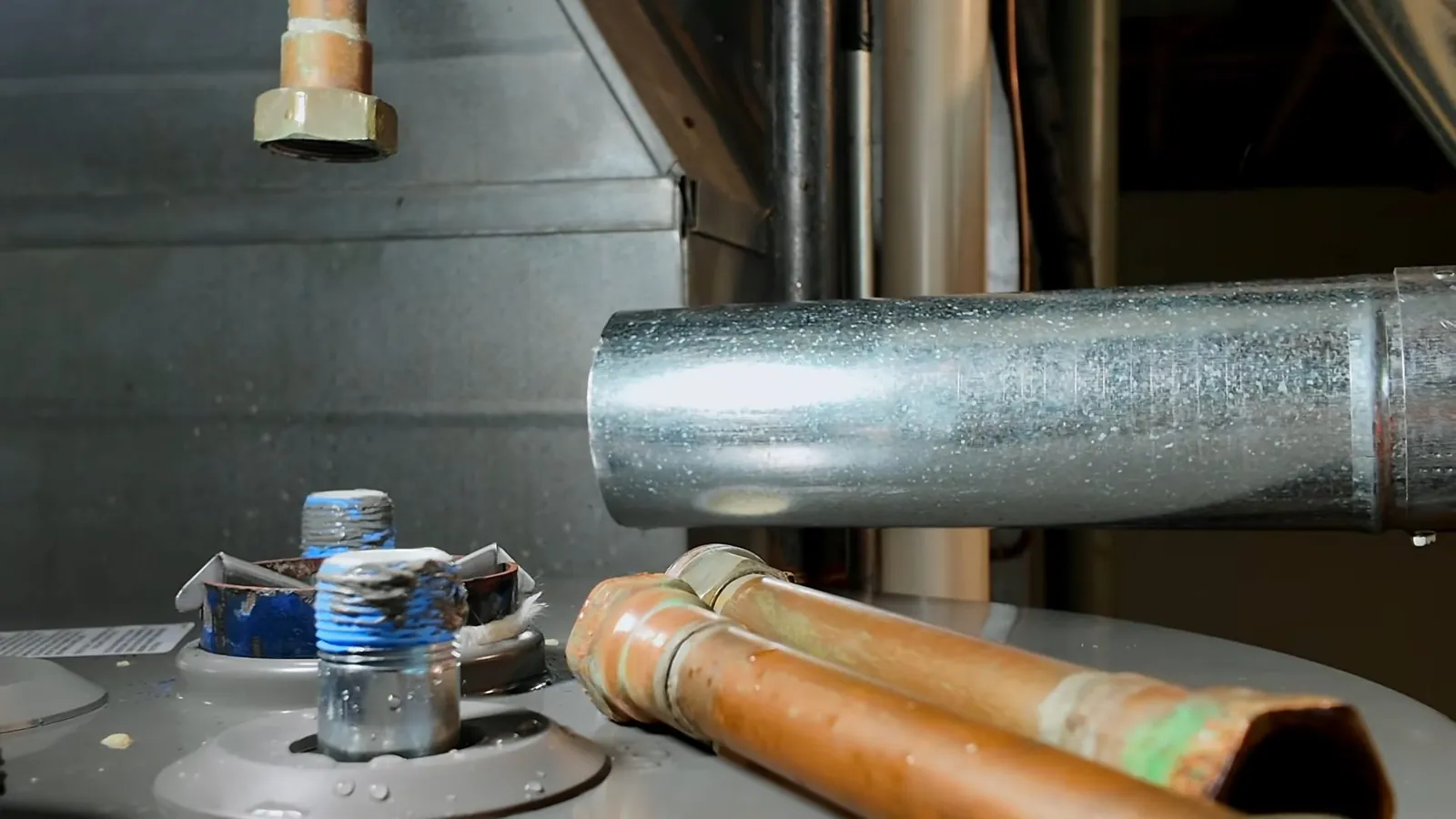 Top of a water heater tank with copper water lines and a galvanized flue pipe