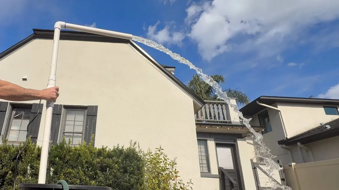 White pipe standing beside a stucco house with a long arc of water spraying out of it