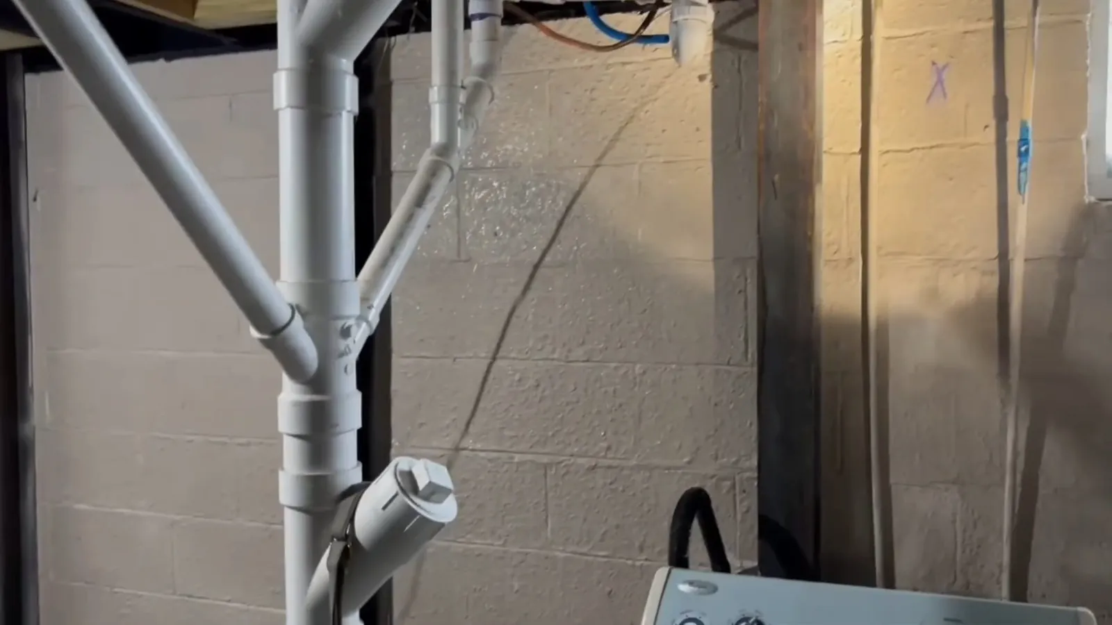 White PVC drain pipes running down a block wall beside an electrical box
